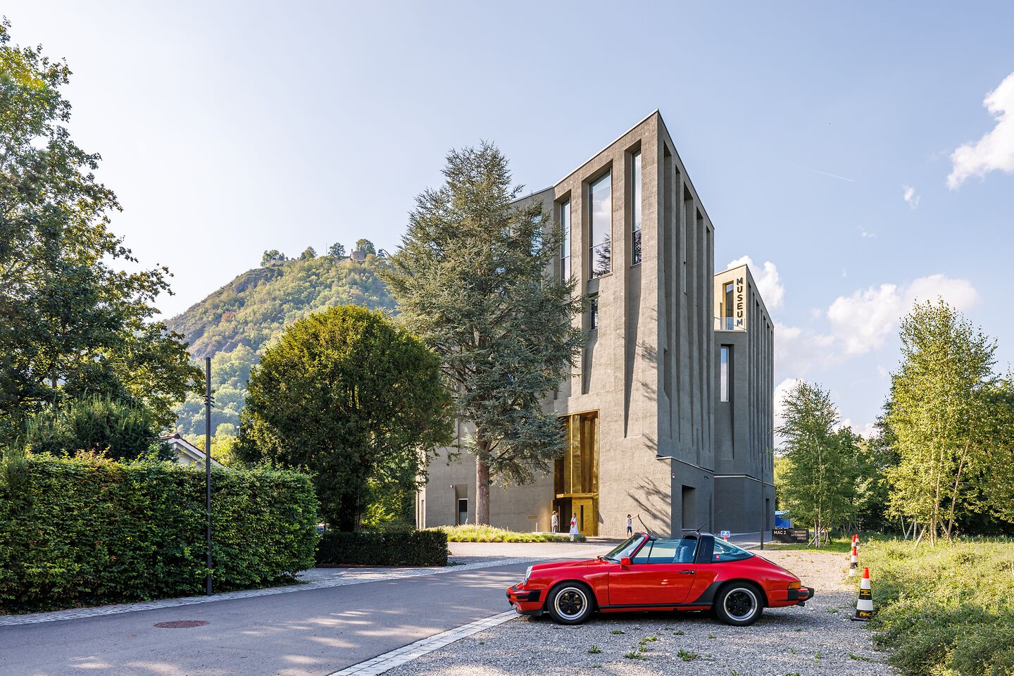 Modernes, graues Museumsgebäude mit schmalen Fenstern in Singen, im Vordergrund ein rotes Cabrio, im Hintergrund ein bewaldeter Hügel.